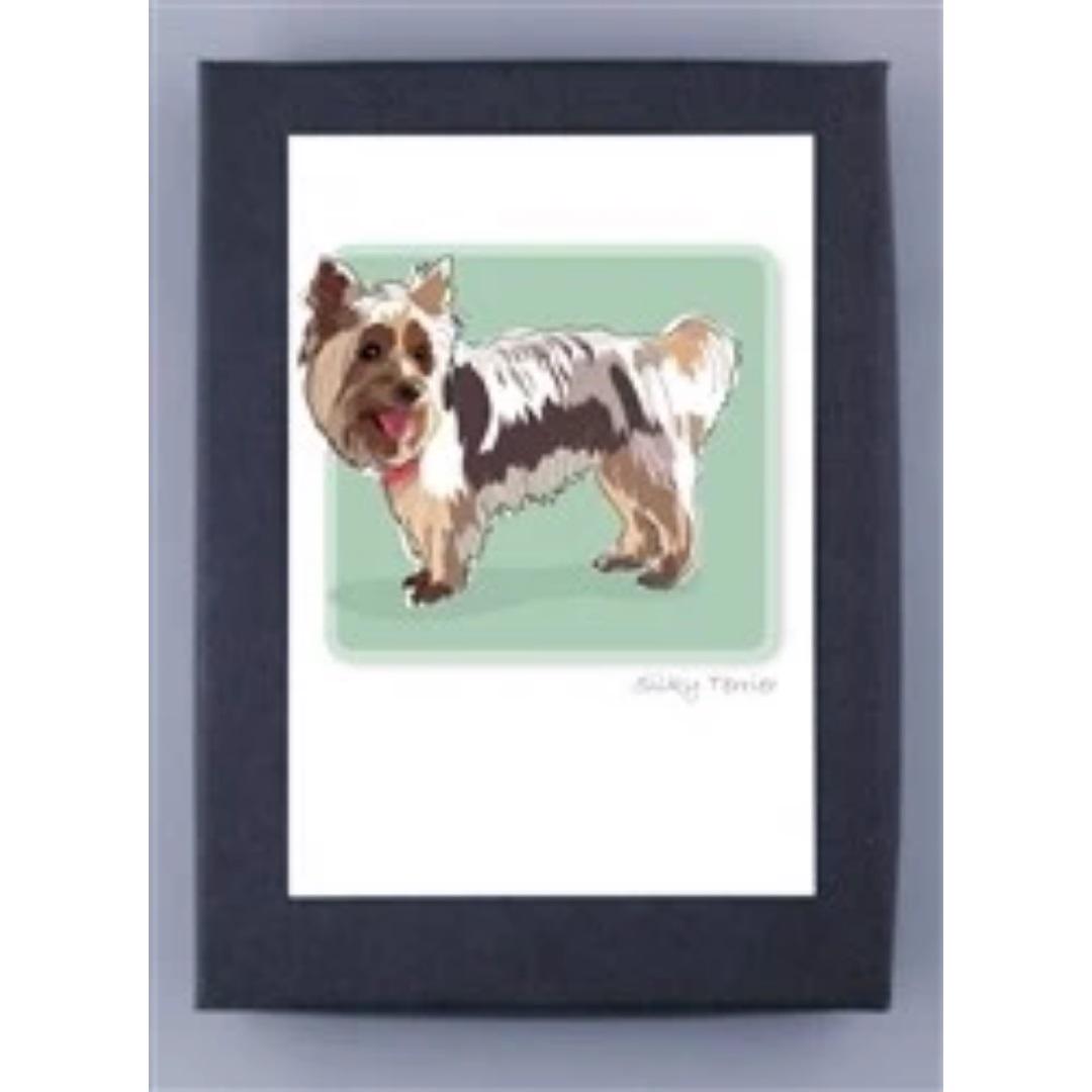 A happy Silky Terrier with a brown and white coat stands on a light green backdrop, tongue out and fluffy tail up. This charming image from PAPER RUSSELLS' "PAPER RUSSELS - SILKY TERRIER BOX NOTES" is framed with a dark border, signed at the bottom, and printed on FSC certified recycled paper.