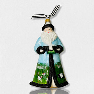 The Fearrington Signature Collection - Handmade Santa Ornament by Joy to the World Collectibles features a bearded figure in a blue robe adorned with farm scenes, including sheep, chickens, and a white fence. This hand-painted keepsake from Fearrington Village is topped with a gold cap and includes a black-and-white striped ribbon for hanging.