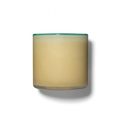 A 6.5 oz LAFCO - French Lilac, Poolhouse candle is displayed in a cylindrical glass container filled with a beige substance. The container features a subtle greenish tint at the rim, evocative of French lilac, and casts a shadow to the right, suggesting the light source is on the left. The background is plain white.