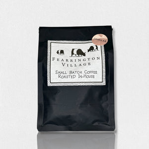 A black bag labeled "Fearrington Signature Collection - Small Batch House Blended Regular Coffee Beans" by Belted Goat features an illustration of three farm animals: a cow, a goat, and a rooster. The text reads "Small Batch Coffee Roasted In-House." A round sticker on the top right corner says "Regular," indicating a blend of beans with a medium-dark roast.