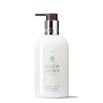 Image of a MOLTON BROWN - HEAVENLY GINGERLILY HAND LOTION bottle. The bottle is white with a silver and brown pump dispenser, featuring a label that reads "Heavenly Gingerlily Hand Lotion" along with branding details and an emblem. This lightweight hand lotion offers a blend of floral lily and warming ginger scents.