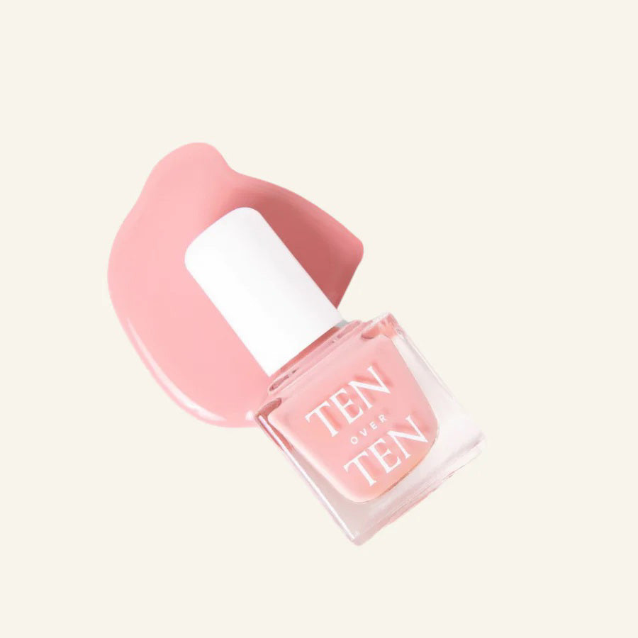 A glass bottle of TENOVERTEN - NAIL POLISH from the brand TEN OVER TEN, featuring a white cap and a dusty pink nail color. The front label displays "TEN OVER TEN" in white uppercase letters. This vegan, eight-free formula ensures both beauty and peace of mind. The background is plain and light-colored.