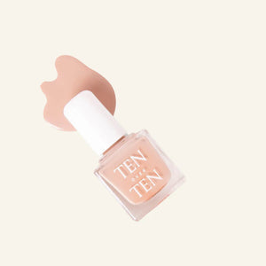 A glass bottle of TENOVERTEN - NAIL POLISH from the brand TEN OVER TEN, featuring a white cap and a dusty pink nail color. The front label displays "TEN OVER TEN" in white uppercase letters. This vegan, eight-free formula ensures both beauty and peace of mind. The background is plain and light-colored.