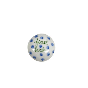 A bespoke, small round porcelain keepsake by ANN MARIE MURRAY, L.L.C., featuring blue polka dots and green cursive text "FIRST LOCK" meticulously hand-painted in the center.