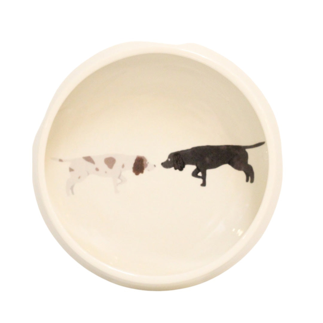 Introducing the NEW SPANIEL DOG BOWL by FENELLA SMITH, a durable dog bowl featuring charming illustrations of two dogs on the inside bottom. One of the dogs is white with brown spots, and the other is solid black. They are depicted facing each other as if about to touch noses, making it an ideal gift for any dog lover.
