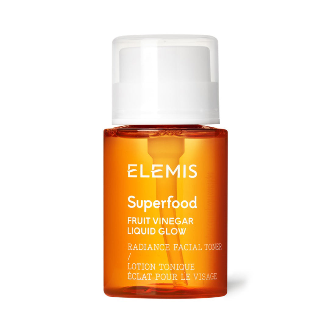 A small, clear orange bottle with a white cap. The label reads &quot;ELEMIS - SUPERFOOD FRUIT VINEGAR LIQUID GLOW&quot; with the brand name &quot;ELEMIS - STEINER.&quot; The French text &quot;Lotion Tonique Éclat Pour Le Visage&quot; is also included. This brightening toner stands against a plain white background.
