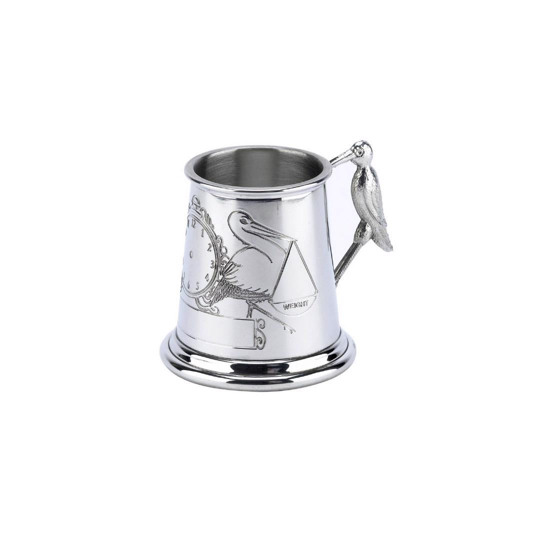 The PEWTER MUG WITH STORK ROLLED DESIGN by CORBELL SILVER COMPANY, INC is a silver metal child's mug featuring a wide base and an engraving of a stork holding a baby bundle. Crafted from English pewter, it includes a small handle detailed with a stork design.