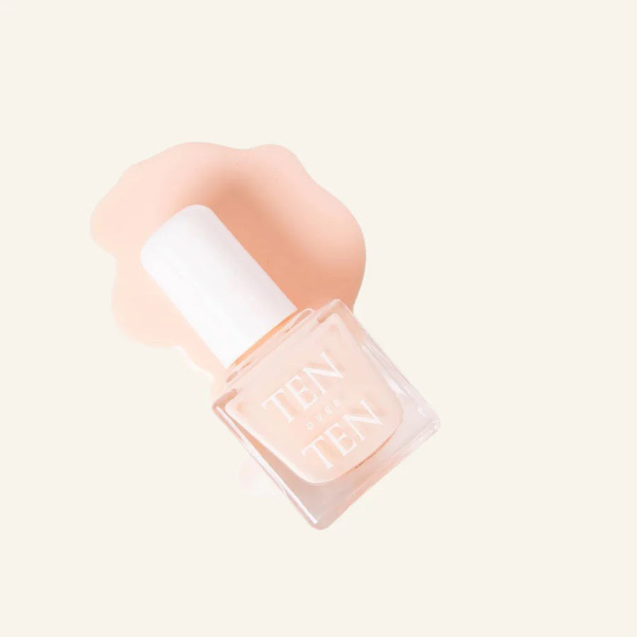 A glass bottle of TENOVERTEN - NAIL POLISH from the brand TEN OVER TEN, featuring a white cap and a dusty pink nail color. The front label displays "TEN OVER TEN" in white uppercase letters. This vegan, eight-free formula ensures both beauty and peace of mind. The background is plain and light-colored.