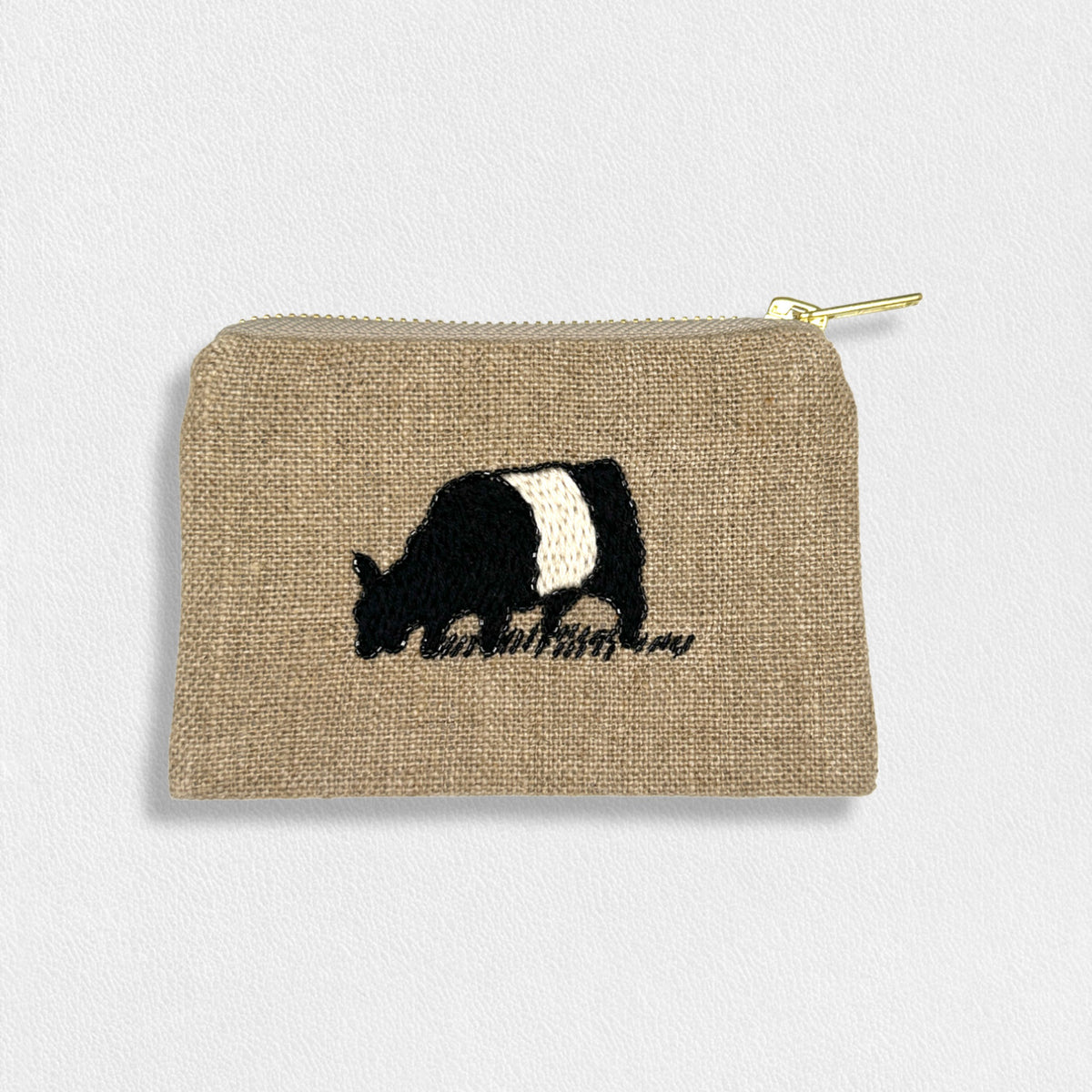 The FEARRINGTON LIFESTYLE COLLECTION - SIGNATURE BELTIE COIN PURSE by CITRUS FASHIONS is a small beige fabric pouch featuring a gold zipper at the top. This linen coin purse highlights an embroidered black and white cow grazing on grass in the center, complemented by delicate hand-stitched details on a plain white background.