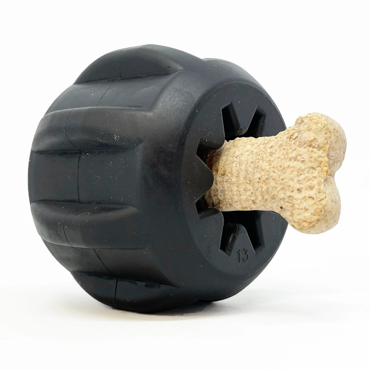 A SODA PUP TREAT HOLDER MAGNUM GEAR (BLACK) with grooved dental ridges encircling it features a bone-shaped treat inserted into the middle. The treat protrudes from this black rubber toy, creating an engaging challenge for the dog to retrieve. The background is white.