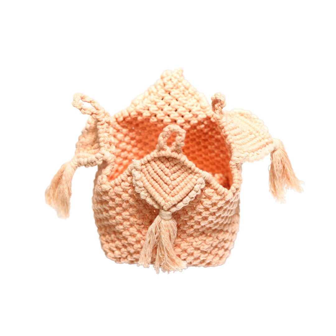 An orange drawstring pouch made of knit fabric hangs against a white background. Handcrafted by artisans, the PANDORA PEONY BOX BAG by BRUNNA CO features braided strings, a small flap on top, and two tassels that dangle from either side, embodying the essence of sustainable fashion accessories.