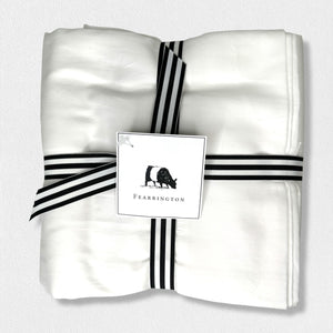 A neatly folded white Frette King Flat Sheet from the Fearrington Lifestyle Bedding Collection is bound with a black and white striped ribbon. A tag attached to the ribbon features the word "Fearrington" and an illustration of a cow, hinting at luxury bedding quality from Frette North America. The background is plain white.