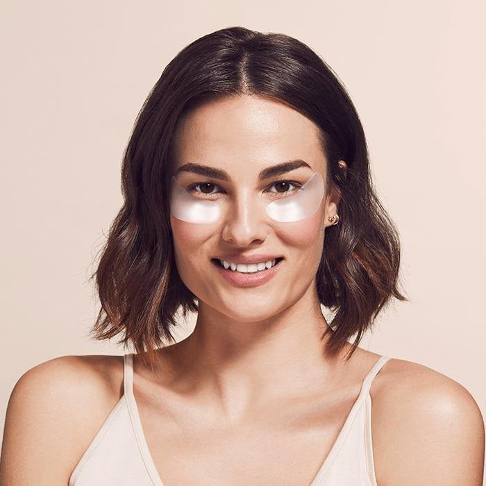 The image shows a product package labeled &quot;SIO EYE AND SMILE&quot; by SIO BEAUTY. The package contains &quot;SIO Eye &amp; Smile Lift Reusable Wrinkle-Smoothing Patches.&quot; Made from medical-grade silicone, these patches target fine lines and wrinkles around the eyes and laugh lines. Next to the package, two white, crescent-shaped patches are displayed on a light pink background.