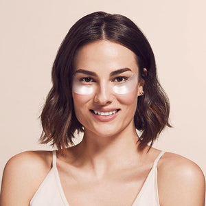 The image shows a product package labeled "SIO EYE AND SMILE" by SIO BEAUTY. The package contains "SIO Eye & Smile Lift Reusable Wrinkle-Smoothing Patches." Made from medical-grade silicone, these patches target fine lines and wrinkles around the eyes and laugh lines. Next to the package, two white, crescent-shaped patches are displayed on a light pink background.