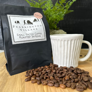 A black bag labeled "Fearrington Signature Collection - Small Batch House Blended Regular Coffee Beans" by Belted Goat features an illustration of three farm animals: a cow, a goat, and a rooster. The text reads "Small Batch Coffee Roasted In-House." A round sticker on the top right corner says "Regular," indicating a blend of beans with a medium-dark roast.