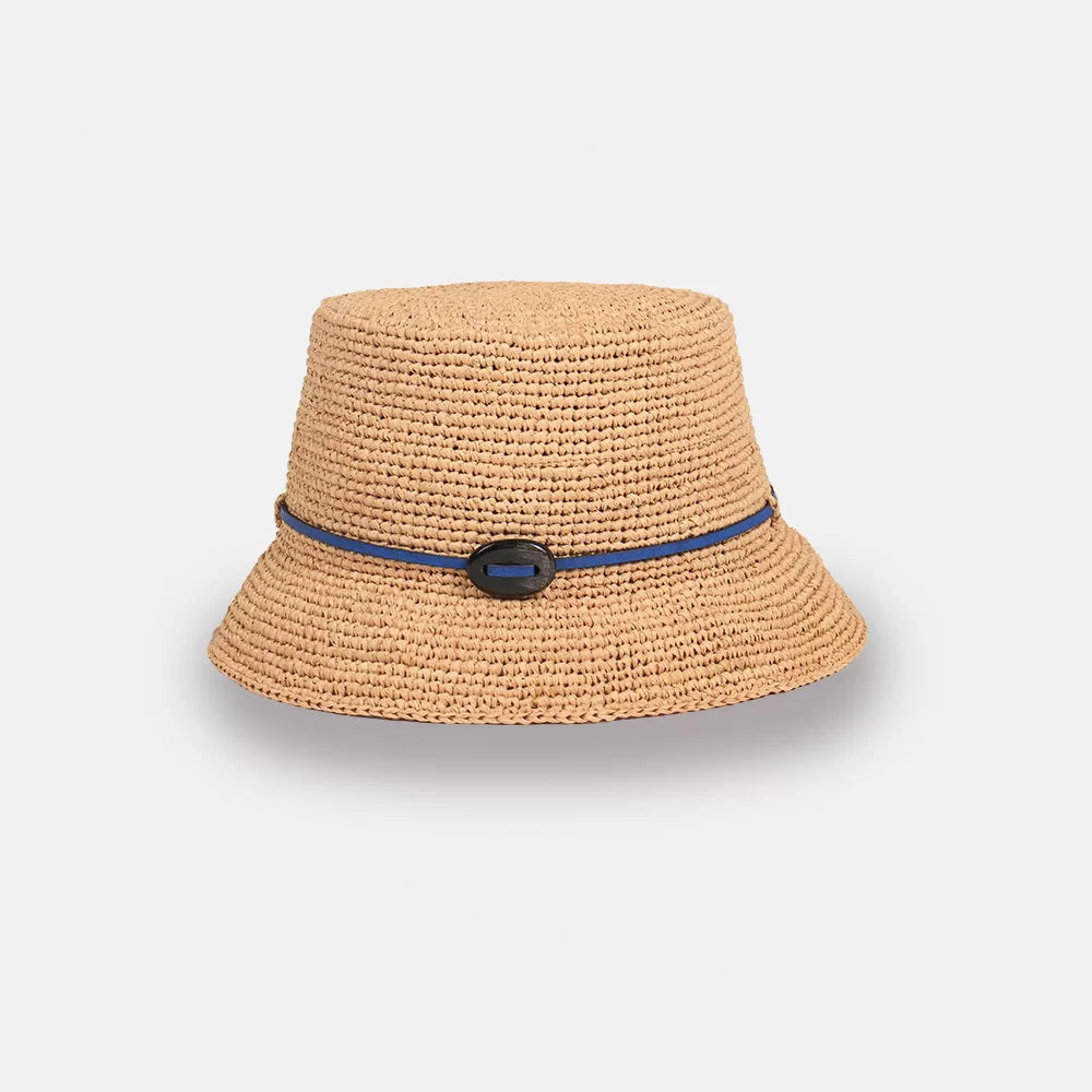 A beige woven bucket hat with a wide brim, featuring a thin dark blue band and a black oval decoration on the front, displayed on a plain light background.