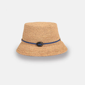 A beige woven bucket hat with a wide brim, featuring a thin dark blue band and a black oval decoration on the front, displayed on a plain light background.