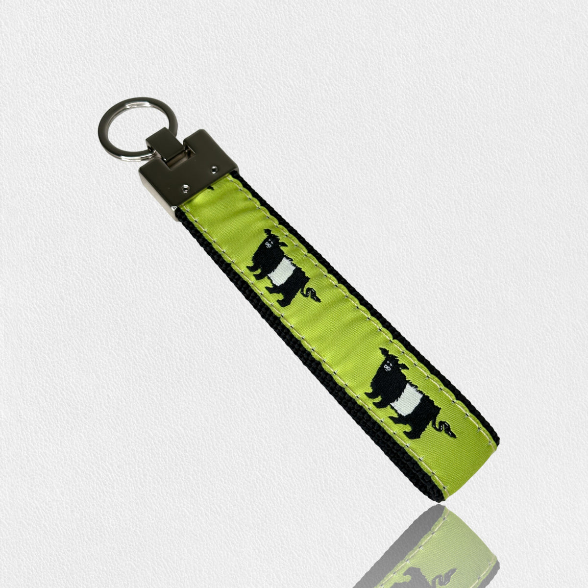The UP COUNTRY &quot;Fearrington Signature Collection - Bespoke Beltie Key Chain&quot; is pictured against a plain white background. The green fabric, adorned with black and white bears that mimic the look of Fearrington&#39;s Beltie cows, features black edging and white stitching, making it a stylish accessory.