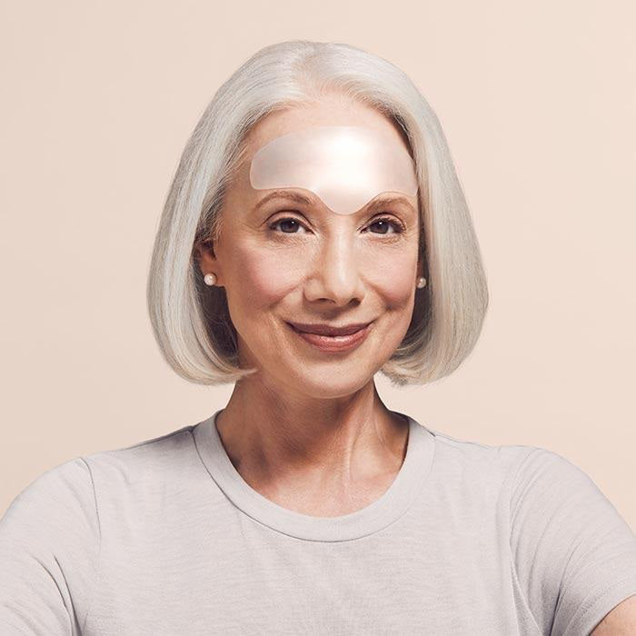 A minimalist arrangement featuring a white marble-patterned notebook, SIO BEAUTY&#39;s transparent curved SIO BROWLIFT resembling medical grade silicone patches, and a small blue envelope. The marble notebook has subtle gray veining, and the blue envelope is centered in front of the notebook.