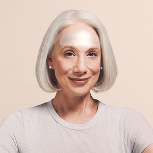 A minimalist arrangement featuring a white marble-patterned notebook, SIO BEAUTY's transparent curved SIO BROWLIFT resembling medical grade silicone patches, and a small blue envelope. The marble notebook has subtle gray veining, and the blue envelope is centered in front of the notebook.