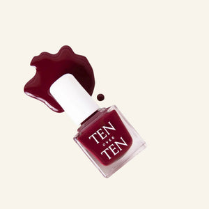 A glass bottle of TENOVERTEN - NAIL POLISH from the brand TEN OVER TEN, featuring a white cap and a dusty pink nail color. The front label displays "TEN OVER TEN" in white uppercase letters. This vegan, eight-free formula ensures both beauty and peace of mind. The background is plain and light-colored.