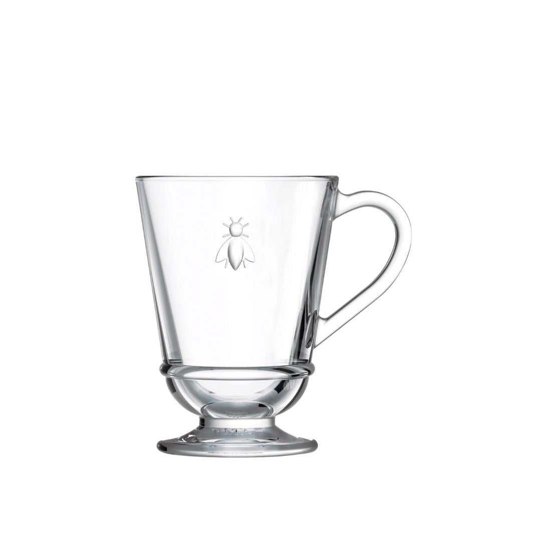 Introducing the BEE MUG by LA ROCHERE: a sophisticated clear glass mug with a handle and a small pedestal base. This exquisite mug showcases an etched design of French bees on the front, making it perfect for elevating your morning routine.