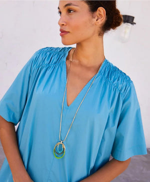 The DIP DYED NECKLACE by MOMONI is a long gold necklace featuring a delicate Venetian chain and interlocking oval pendants at the center. Made in Italy, the pendants showcase a layered look with gold, white, and coral colors. The necklace is displayed flat on a white background.