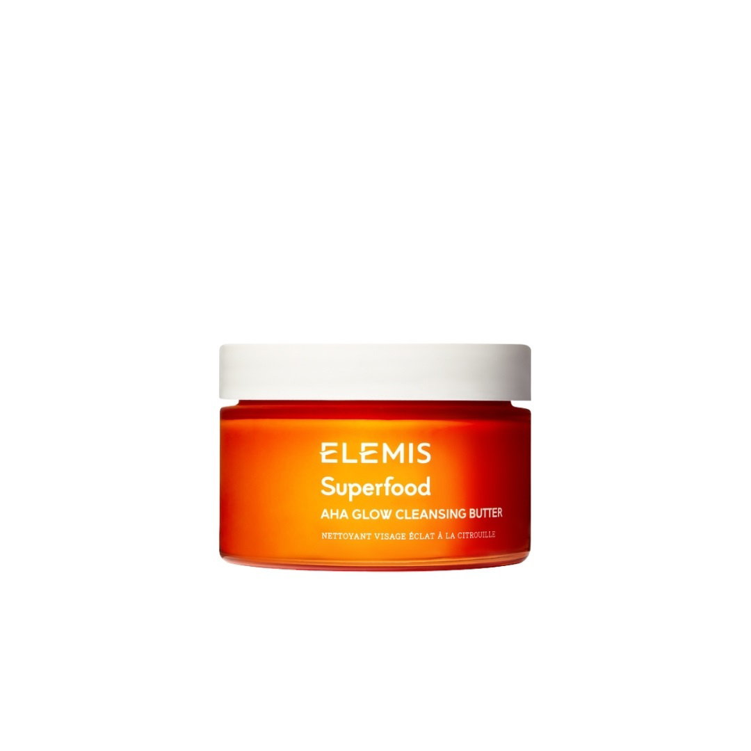 A bright orange jar with a white lid, labeled &quot;ELEMIS - SUPERFOOD AHA GLOW CLEANSING BUTTER&quot; in white text, from the brand ELEMIS - STEINER, featuring nourishing Mango Butter and Pumpkin enzymes. The jar is centered against a plain white background.