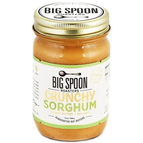 A jar of Big Spoon Roasters - Peanut Crunchy Sorghum Nut Butter. The jar features a golden lid with &quot;Big Spoon Roasters&quot; inscribed on top. Its label is predominantly white and green, emphasizing the handmade quality, sea salt, and coarse-ground texture with fresh-roasted split peanuts for an ultra-crunchy experience.
