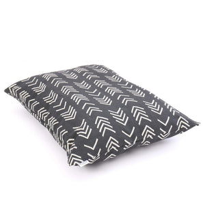 Close-up of The Foggy Dog's DOG BED (S, MODERN MUD CLOTH BLACK) with a dark gray background and white geometric arrow patterns. The fabric texture is visible, and the pillow is positioned at an angle, showcasing the stitching. Made in the USA with an eco-friendly insert, this boho minimalist dog bed adds style to any space.