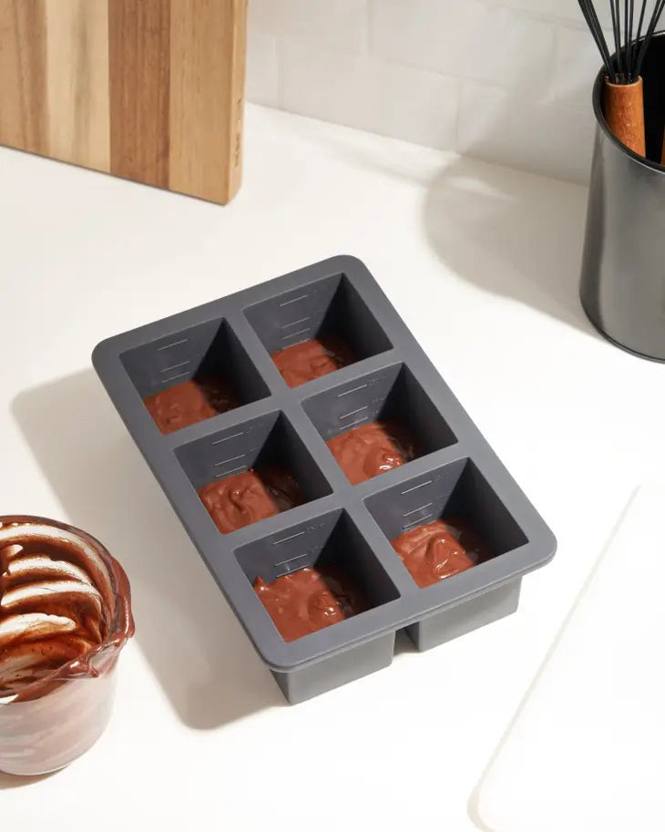 A W&amp;P Design branded Cup Cube Freezer Tray (6) with a transparent lid is displayed against a white background. The packaging features an image of square frozen cubes containing herbs and fruit. Crafted from food-safe silicone, the tray is designed to make large, gourmet ice cubes.
