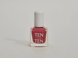 A glass bottle of TENOVERTEN - NAIL POLISH from the brand TEN OVER TEN, featuring a white cap and a dusty pink nail color. The front label displays "TEN OVER TEN" in white uppercase letters. This vegan, eight-free formula ensures both beauty and peace of mind. The background is plain and light-colored.