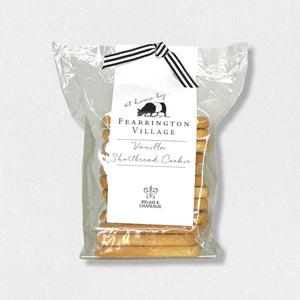 A stack of buttery and crisp vanilla shortbread cookies is displayed on a black serving board in front of a clear package labeled "Fearrington House Signature Collection - Housemade Vanilla Shortbread Cookies" with a black and white striped ribbon tie at the top. These delectable treats could easily be found at The Fearrington House Restaurant.