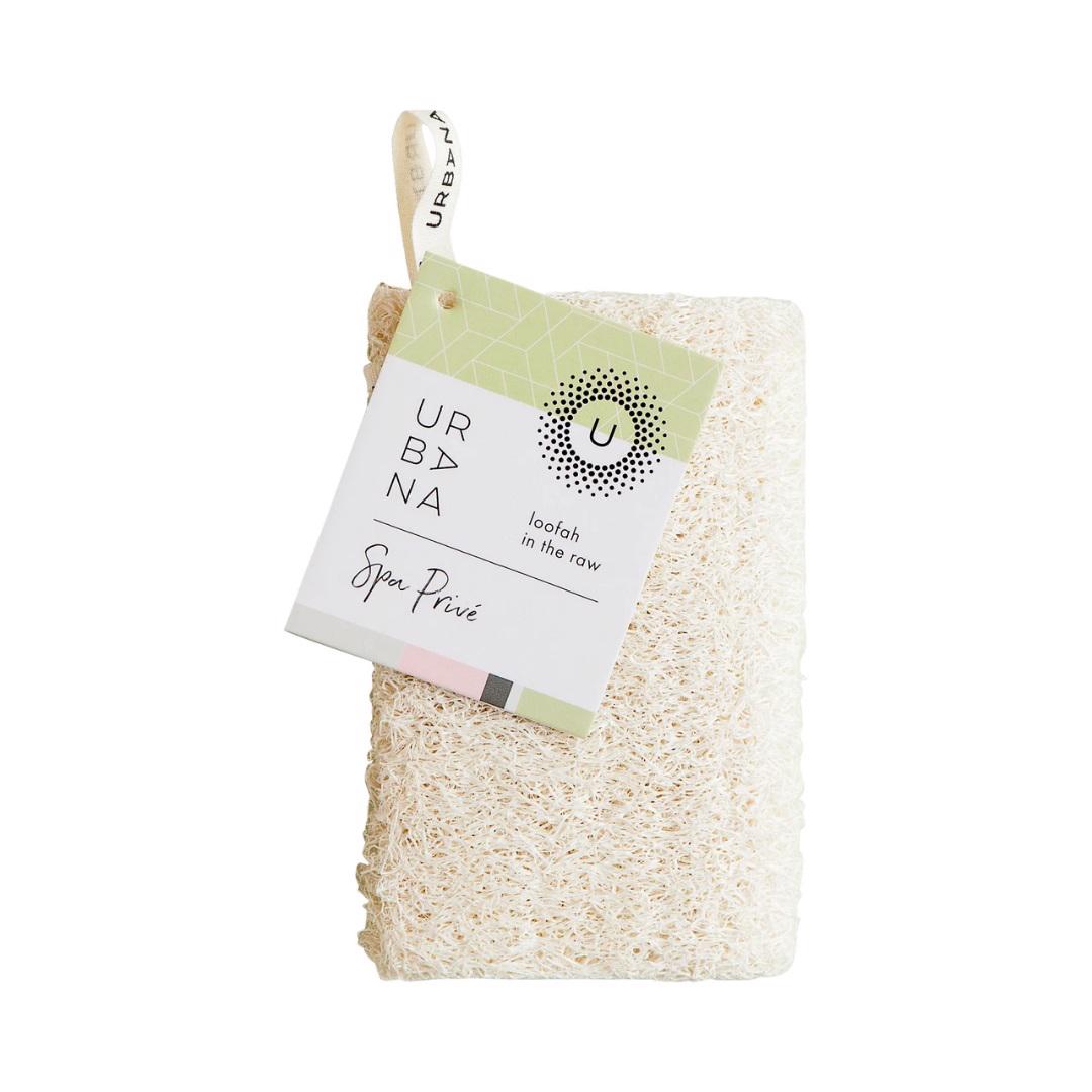 Displayed is a natural loofah sponge in a rectangular shape. It features an Urbana Spa Privé tag at the top, indicating the brand and product details. Branded as LOOFAH IN THE RAW by EUROPEAN SOAPS, LLC, this exfoliating loofah has a rough, fibrous texture that makes it perfect for personal care and natural bath products.