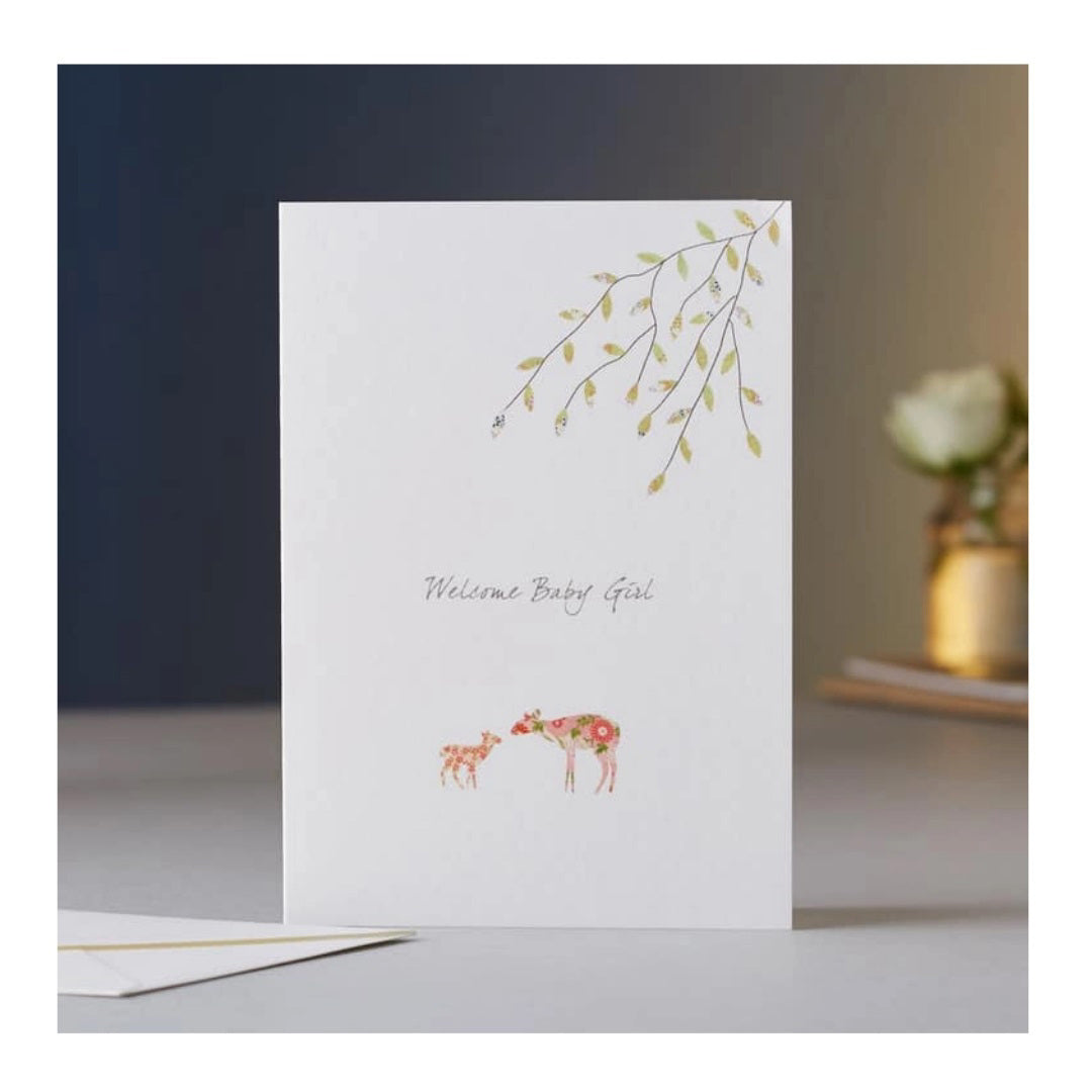 Introducing the ELOISE HALL - NEW BABY GIRL CARD from ELOISE HALL LTD. This luxurious greeting card features the title "Welcome Baby Girl" in an elegant script font. The card showcases a beautifully illustrated mother deer and baby deer, both adorned with delicate floral patterns. Overhanging branches with green leaves are depicted in the top right corner, adding a charming touch to this exquisite piece of stationery.