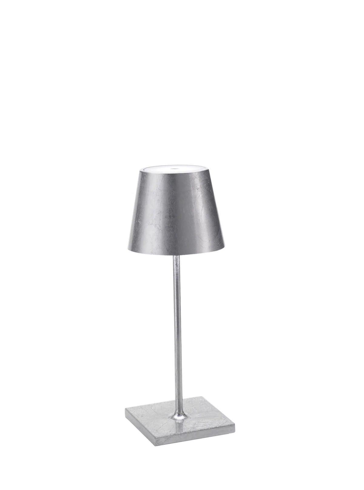 Introducing the POLDINA PRO MINI SILVER LEAF CORDLESS LAMP by ZAFFERANO AMERICA, LLC—a minimalist silver table lamp with a cylindrical shade and slender, vertical stand attached to a square base. Its sleek metallic finish adds a modern touch to your décor, while its cordless illumination makes it perfect for both indoor and outdoor use.