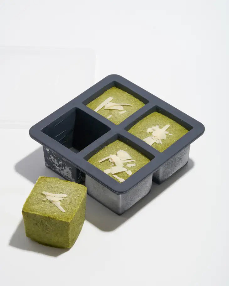 A gray, food-safe W&amp;P - CUP CUBE FREEZER TRAY by W&amp;P DESIGN holds four cube-shaped green desserts with intricate white leaf-like patterns on top. One of the cubes is positioned outside the kitchen tool on a white surface, showcasing its sides and top pattern. The mold casts a shadow to the left.