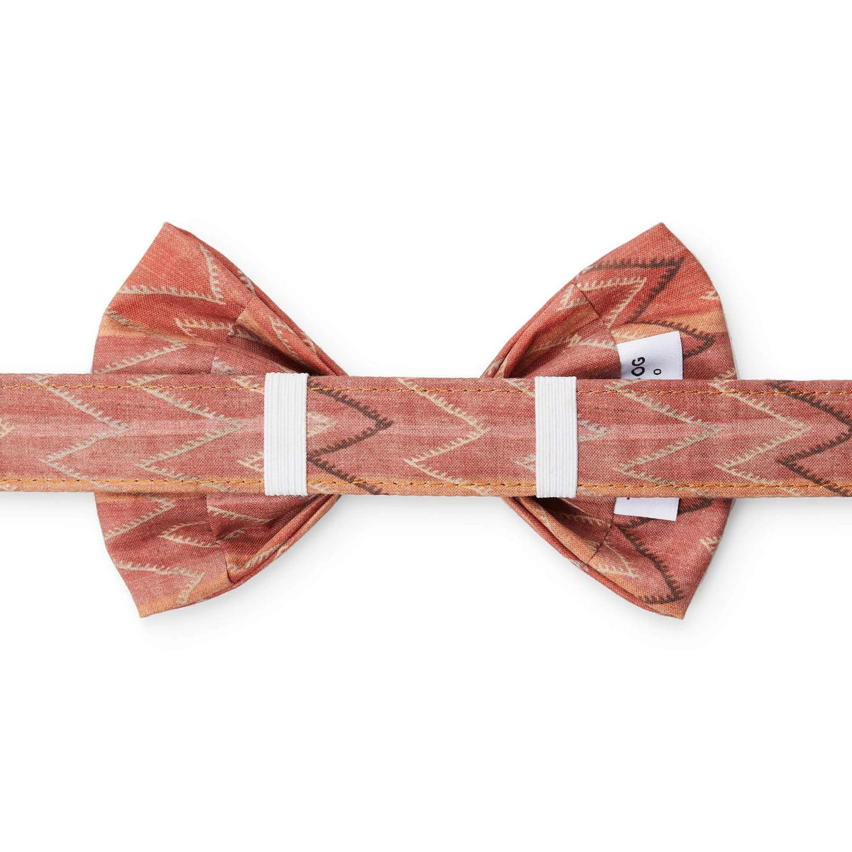 The DOG BOW TIE (STANDARD, ST. FRANK CHEVERON KILIM) by THE FOGGY DOG is a stylish accessory made from rust-colored, textured fabric featuring a white zigzag pattern. This American-made dog bow tie is neatly tied to showcase its elegant design and composition against a solid white background, emphasizing the detailed patterns and rich color.