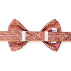 The DOG BOW TIE (STANDARD, ST. FRANK CHEVERON KILIM) by THE FOGGY DOG is a stylish accessory made from rust-colored, textured fabric featuring a white zigzag pattern. This American-made dog bow tie is neatly tied to showcase its elegant design and composition against a solid white background, emphasizing the detailed patterns and rich color.