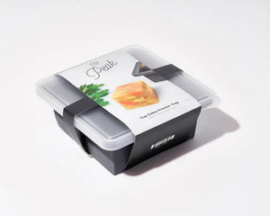 A gray, food-safe W&P - CUP CUBE FREEZER TRAY by W&P DESIGN holds four cube-shaped green desserts with intricate white leaf-like patterns on top. One of the cubes is positioned outside the kitchen tool on a white surface, showcasing its sides and top pattern. The mold casts a shadow to the left.