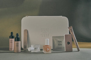 The TENOVERTEN - THE MANICURE KIT, by TEN OVER TEN, is showcased alongside various cosmetic items. The beige pouch features the text "TEN OUT OF TEN" and includes a Rose Oil dropper bottle, The Foundation, a cuticle eraser, a nail file, clear and white nail polish, a square bottle, a small box, and a tube.