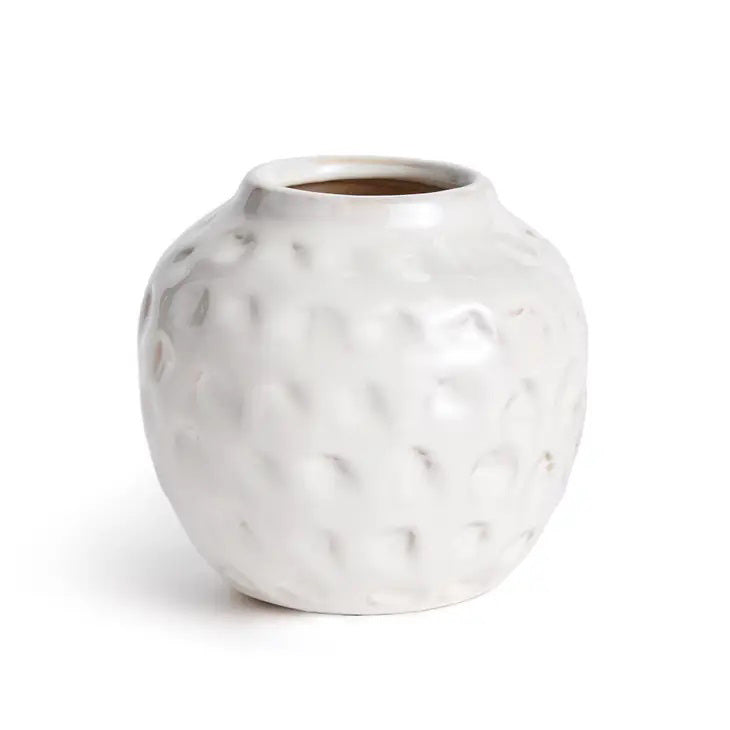 The NAPA HOME AND GARDEN - MARIAH ORGANIC SMALL VASE is a white, round ceramic piece with a textured, dimpled surface and artisan feel. Its narrow top and hand-applied glaze create a glossy finish accentuated by a plain light background.