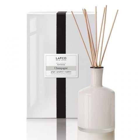 The LAFCO - CHAMPAGNE, PENTHOUSE DIFFUSER by Lafco features a sophisticated white ceramic bottle filled with fragrant oil infused with hints of grapefruit. This set comes in elegant packaging adorned with a sleek black stripe and includes several natural reeds for dispensing the scent.
