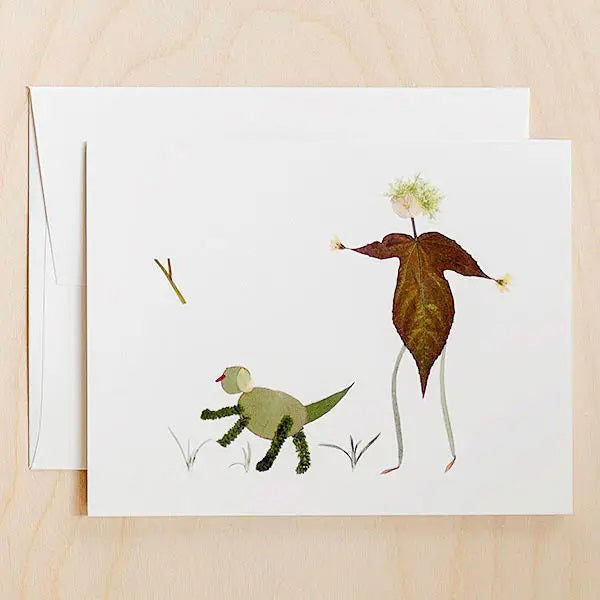 Introducing the FETCH CARD by PETAL PEOPLE PRESS – a greeting card that showcases a minimalist illustration made from pressed botanicals. It features a person created from a large leaf and thin stems, playing fetch with a dog crafted using small green leaves and moss. The high-resolution digital print ensures every detail is crisp against the white background.