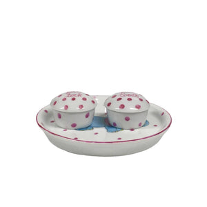 Introducing the TOOTH AND LOCK ELEPHANT (PINK) by ANN MARIE MURRAY, L.L.C., a bespoke porcelain set that includes a beautifully crafted plate and two small lidded containers. The plate showcases a hand-painted blue elephant with pink ears playing with a colorful ball, all surrounded by charming pink polka dots. The dotted lidded containers are thoughtfully labeled "first lock" and "first tooth.