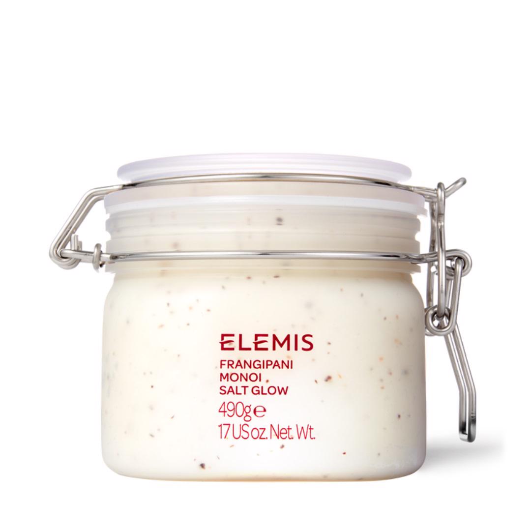 A jar of ELEMIS - FRANGIPANI MONOI SALT GLOW from ELEMIS - STEINER, containing 490 grams (17 ounces) of product. The jar has a white lid secured with a metal latch and is filled with a white, speckled exfoliating salt scrub enriched with Tahitian Monoi Oil. The label on the jar is red and provides product details.