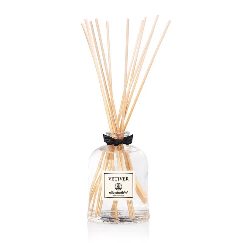 A clear Italian glass container labeled &quot;VETIVER DIFFUSER&quot; by E WIGHTMAN &amp; CO is filled with a liquid and several long, thin wooden reeds extending out of the top. This environmentally friendly diffuser features a small black ribbon at the neck, offering a long-lasting fragrance for any room.