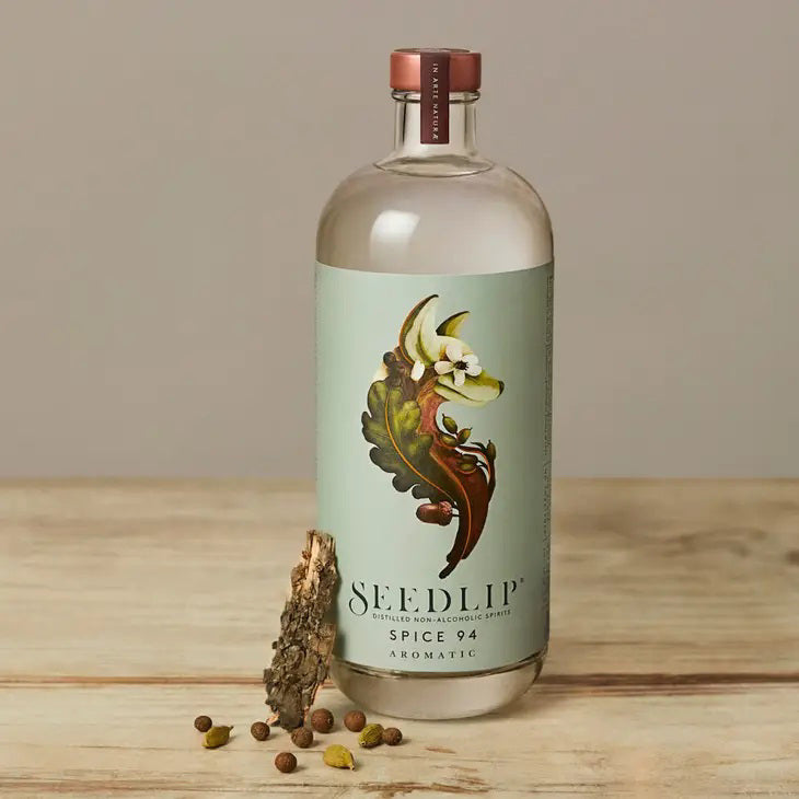 A clear bottle of SEEDLIP - SPICE 94 NON ALCOHOLIC SPIRIT by SEEDLIP DRINKS, featuring a light green label with leaves and spices, plus a copper-colored cap, displayed against a white background.