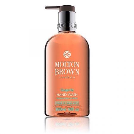 A pump bottle of Molton Brown Heavenly Gingerlily Hand Wash with white lily extract. The transparent bottle displays the orange liquid inside, while the label features details like "300ml" and "Made in England." The sleek pump dispenser is accented in silver and black.