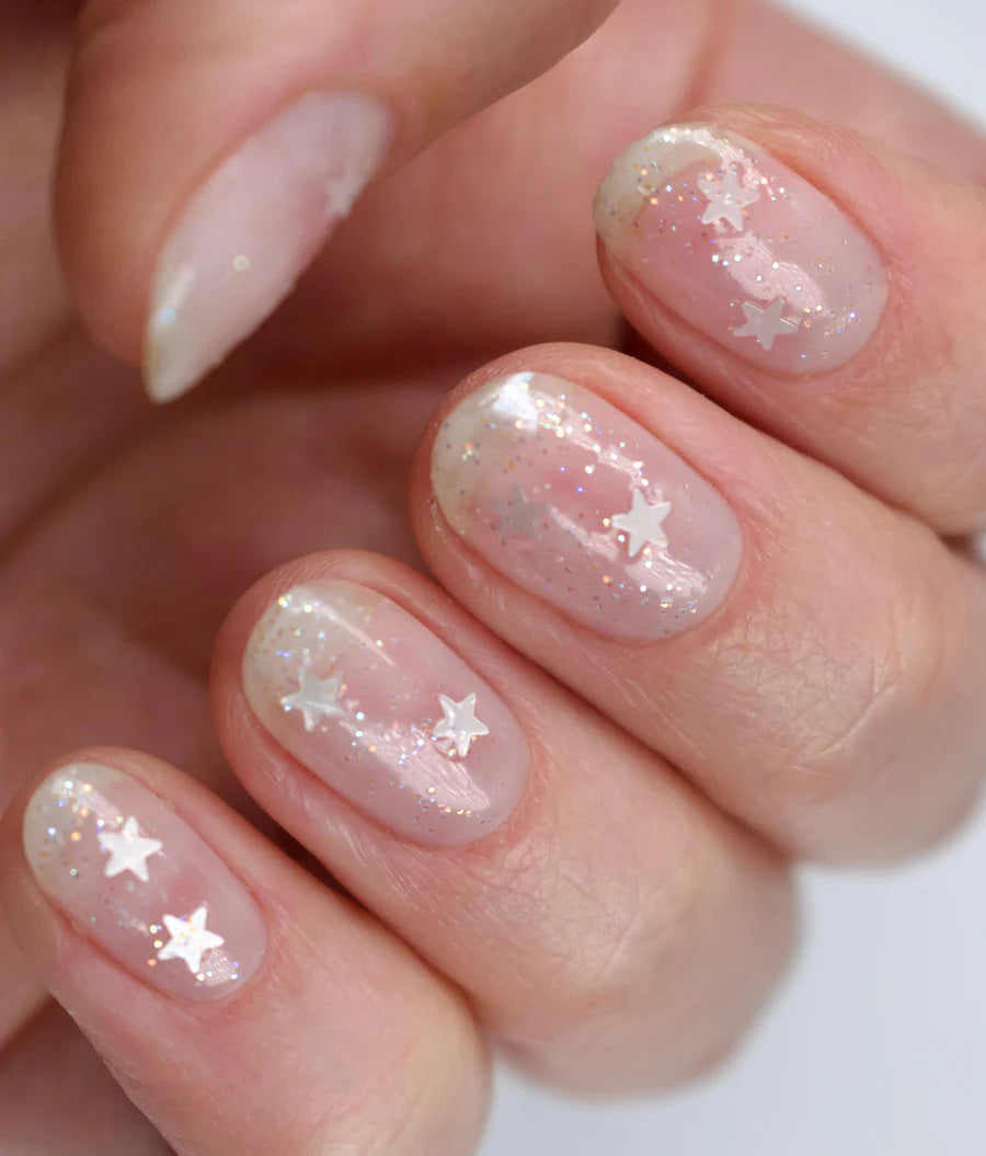 A glass bottle of TENOVERTEN - NAIL POLISH from the brand TEN OVER TEN, featuring a white cap and a dusty pink nail color. The front label displays "TEN OVER TEN" in white uppercase letters. This vegan, eight-free formula ensures both beauty and peace of mind. The background is plain and light-colored.